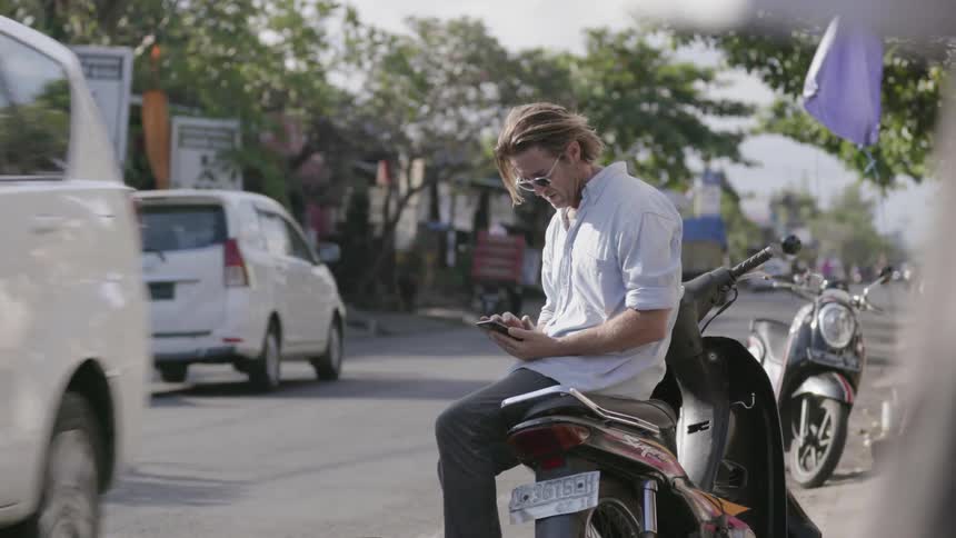 A man sits on a scooter on the busy street