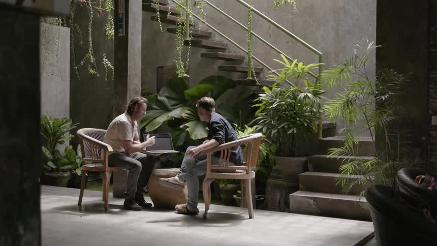 Two men look at a laptop in a courtyard