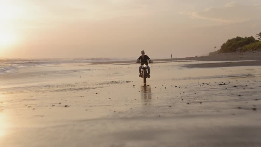 Man rides motorcycle along beach
