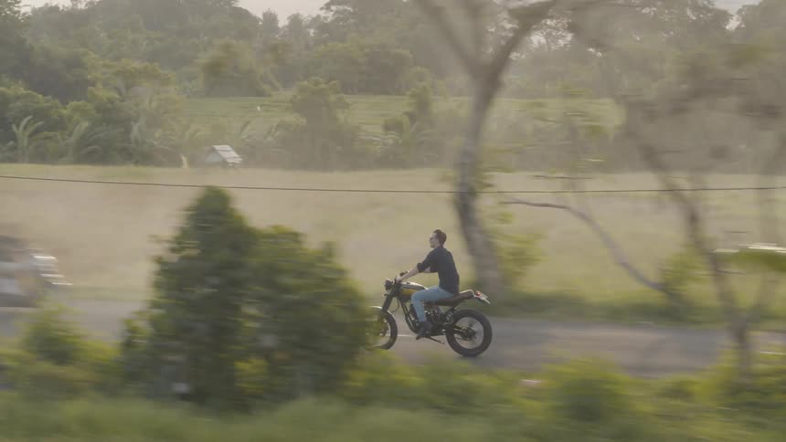A man is riding a motorcycle through a rural community in an asian country in daylight