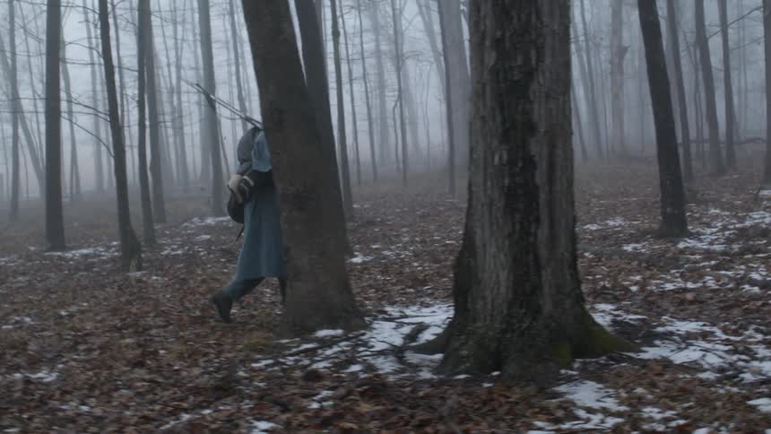 A soldier carries a rifle in a foggy forest