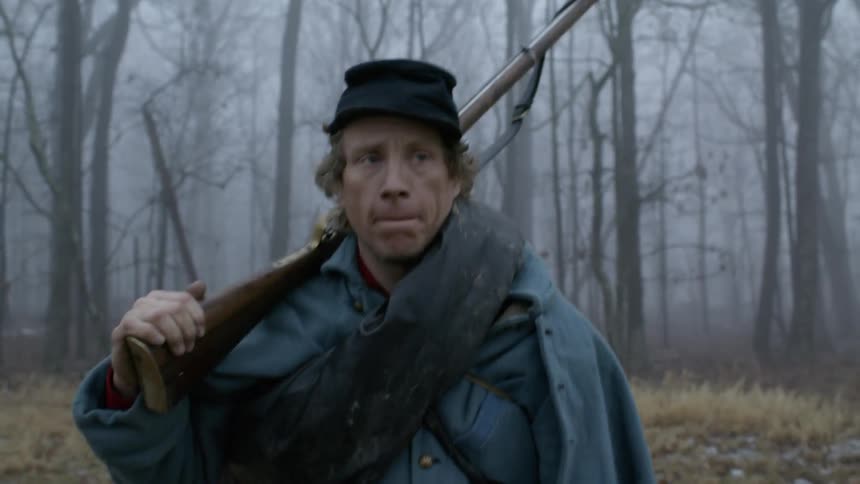 A soldier carries a rifle in a forest