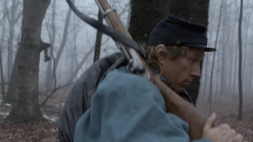 A soldier carries a rifle in a foggy forest