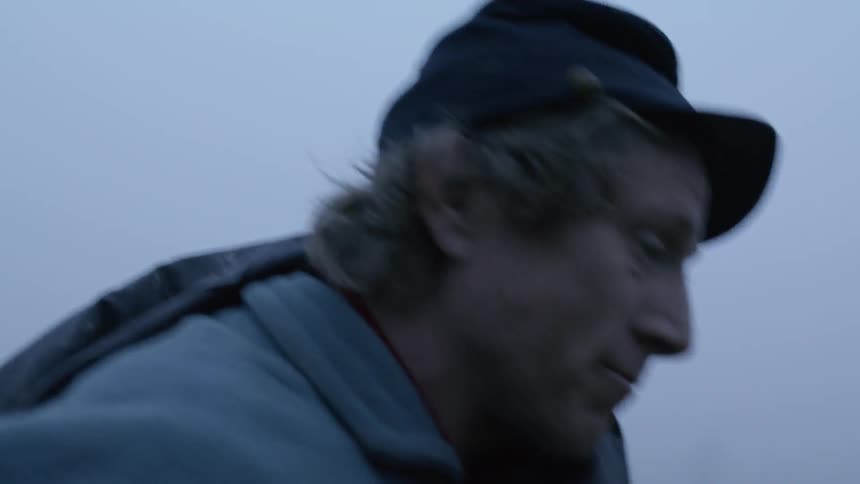 A soldier puts his cap on and walks through a foggy field