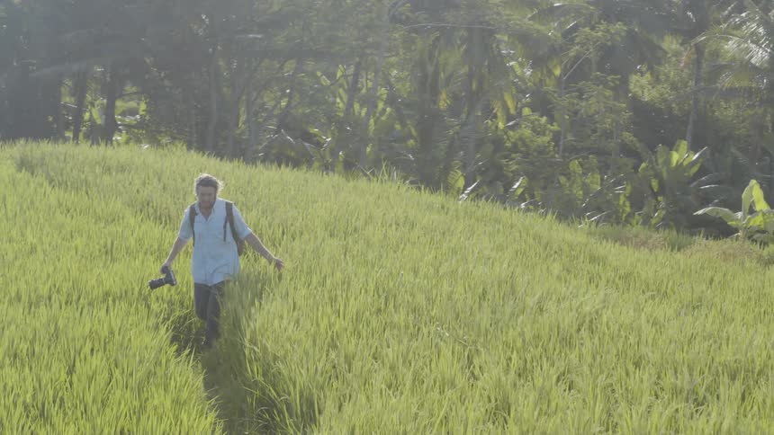 A man walks through a grassy field carrying a camera