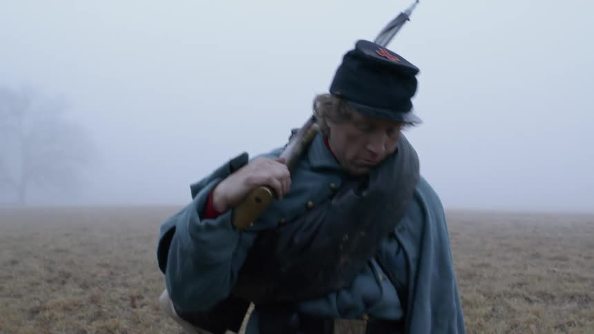 A soldier carries a rifle in a foggy field