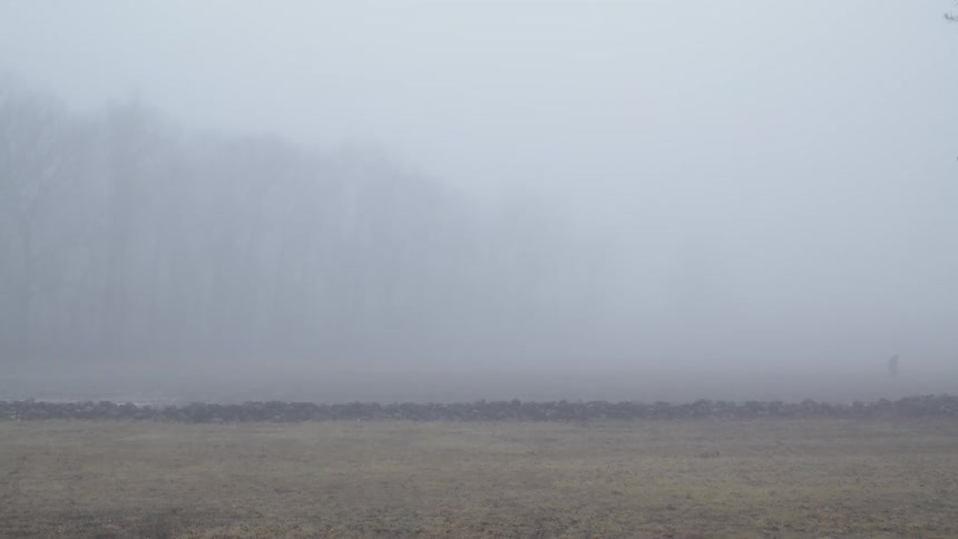 A soldier is walking across a field on a foggy day