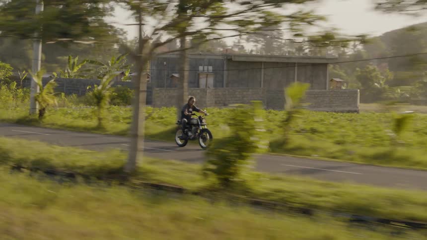 A man is riding a motorcycle through a rural community in an asian country in daylight