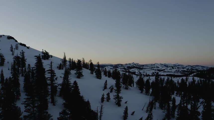 A moody aerial flight over trees and mountains at dusk