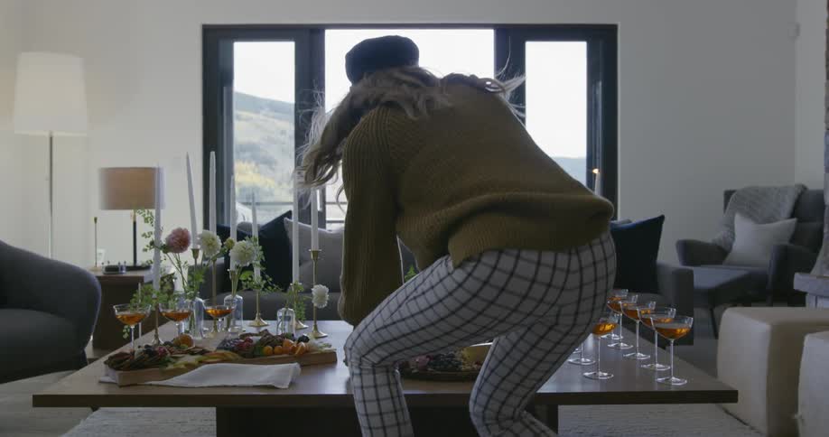 A woman kneels down and adjusts a platter of food on a coffee table