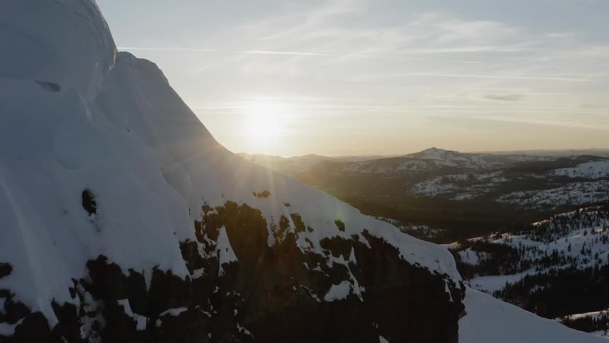 Slow aerial flight past snowy ridge line into the sunset