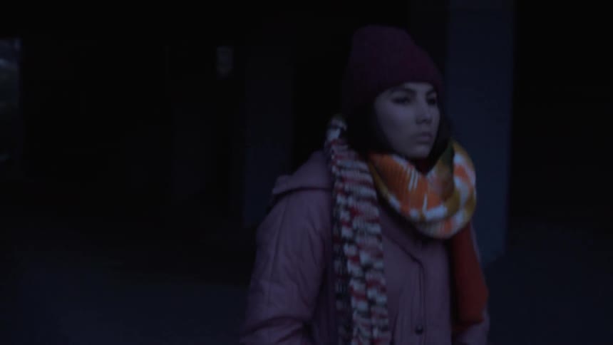 A woman is using using her cellphone as she walks through a tunnel on a cold morning