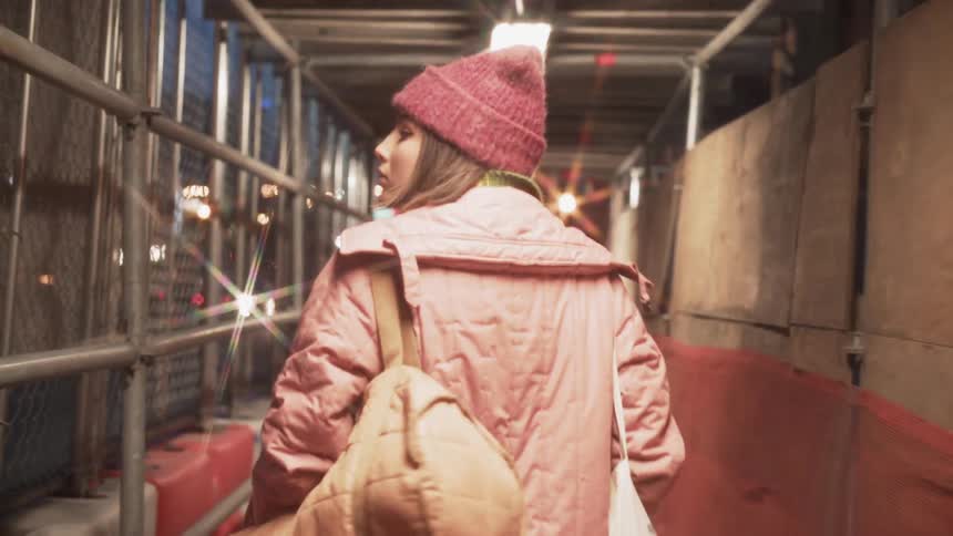 A woman is walking under the scaffolding by a building