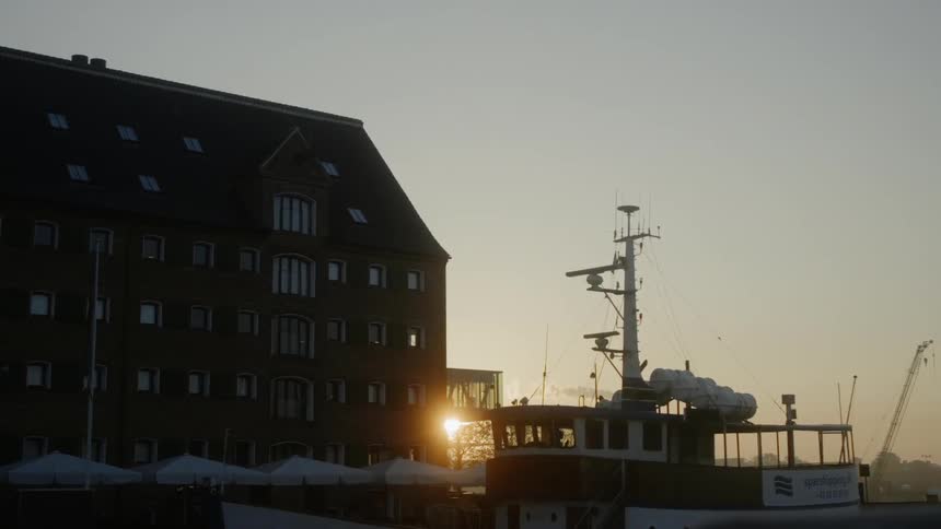 The sun sets behind a building at boat