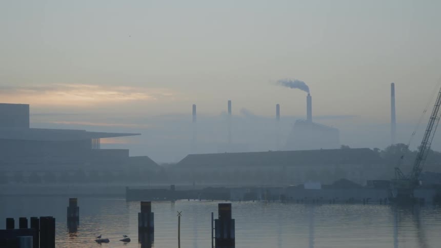 Smoke billows from a factory smokestack at sunset
