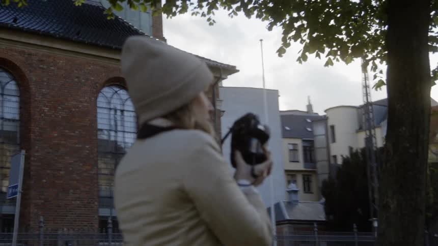 A woman takes a photograph on a city sidewalk