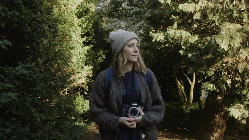 A woman is carrying a camera as she walks through a park during the day