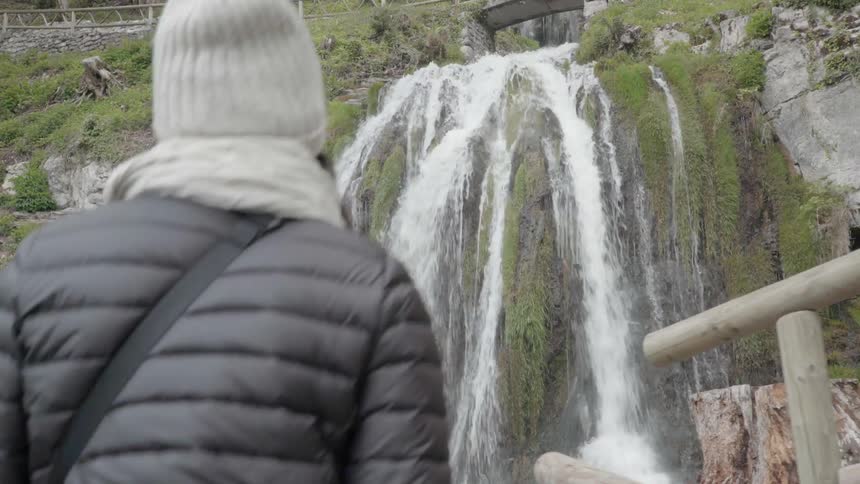 A woman walks on a deck overlooking a waterfall