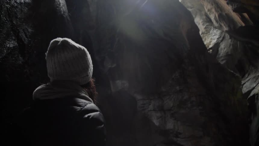 A woman looks around in the dark cave