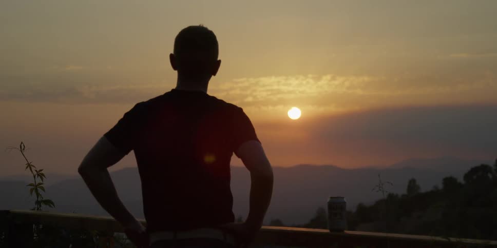 A man stands atop a hill looking at the sun