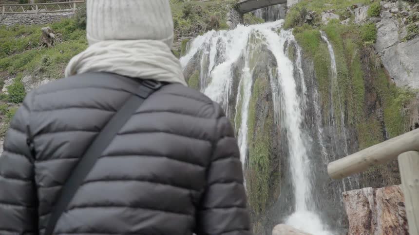 A woman walks toward a waterfall