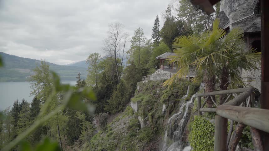 A waterfall is cascading over a cliff below a path on a cloudy day