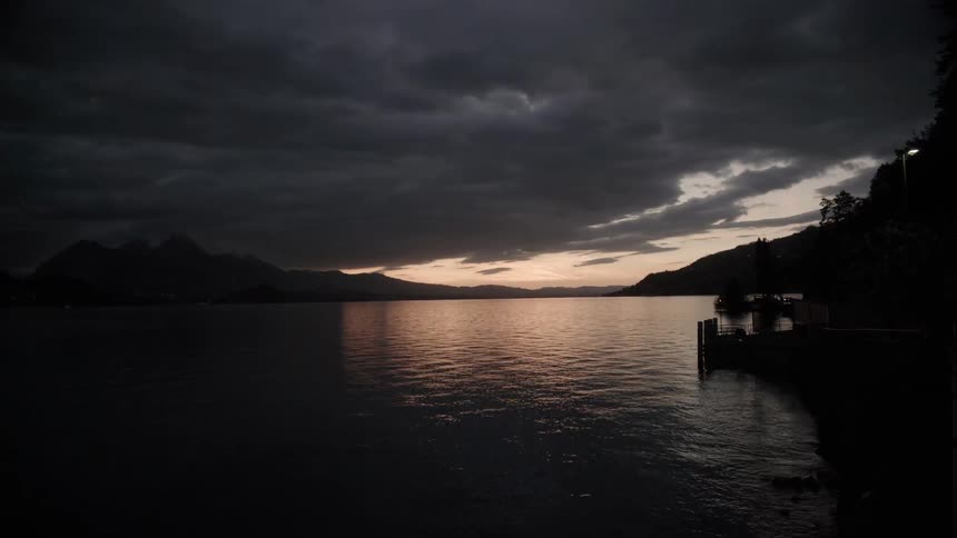 The sun sets behind a mountain lake