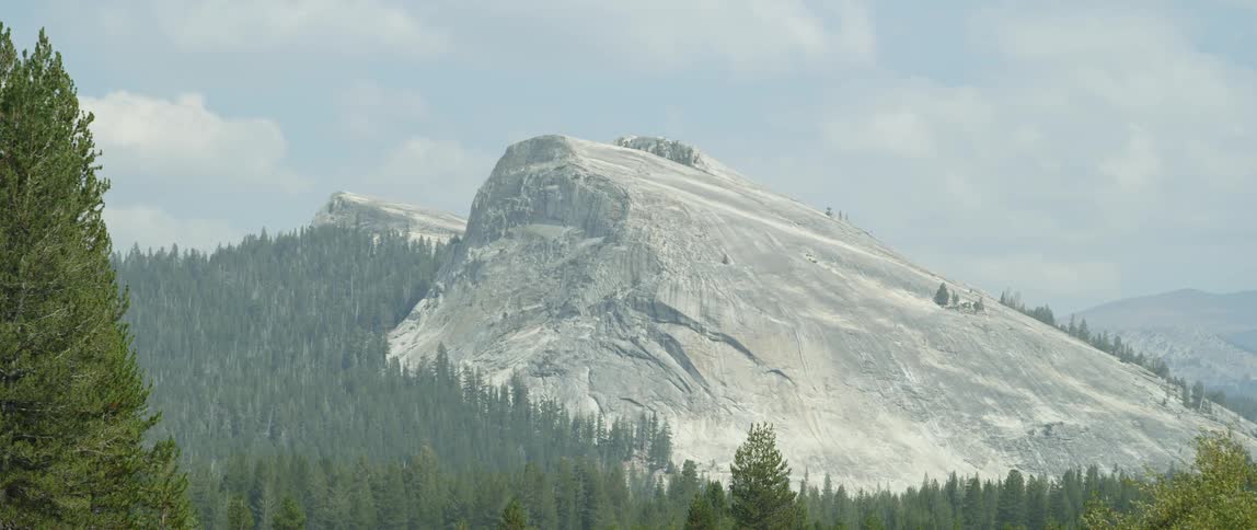 Large rock sits surrounded by trees under a cloudy blue sky