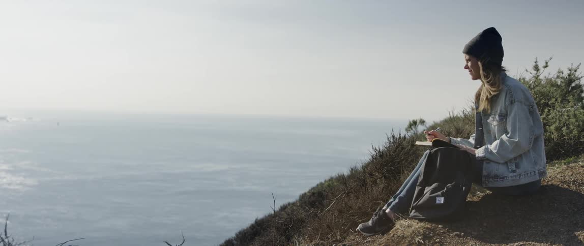 Woman writes in a notebook while overlooking a beach
