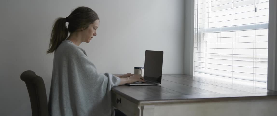 A woman is sitting by the window using her laptop