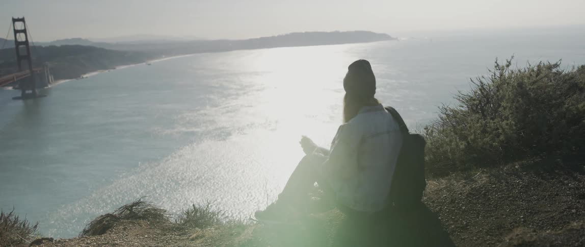 A woman sits down by the cliff overlooking the water