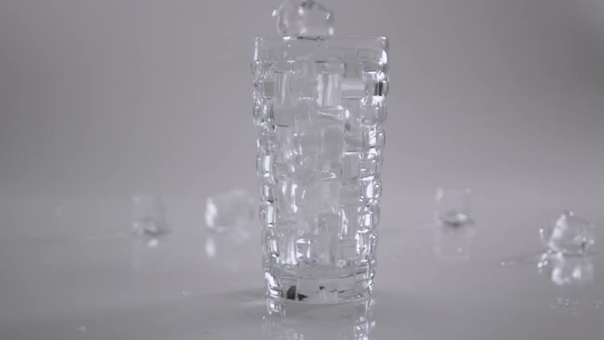 Ice cubes fall into a glass and onto a table