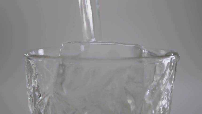 Water pours over ice cubes in a clear glass