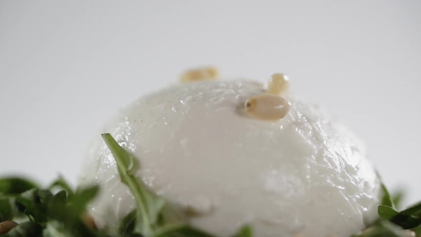 Pine nuts are dropped onto a ball of soft cheese on a bed of greens
