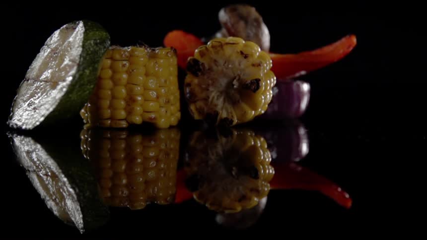 A corn cob rolls towards cooked vegetables