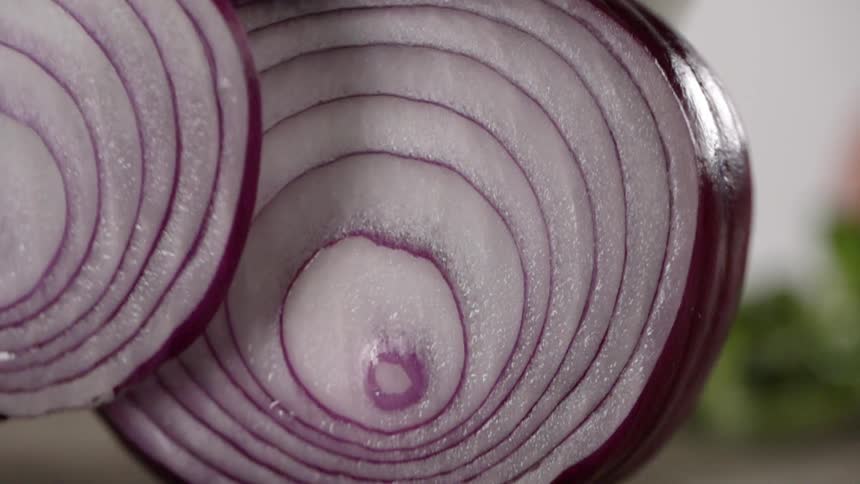 A knife cuts through a red onion