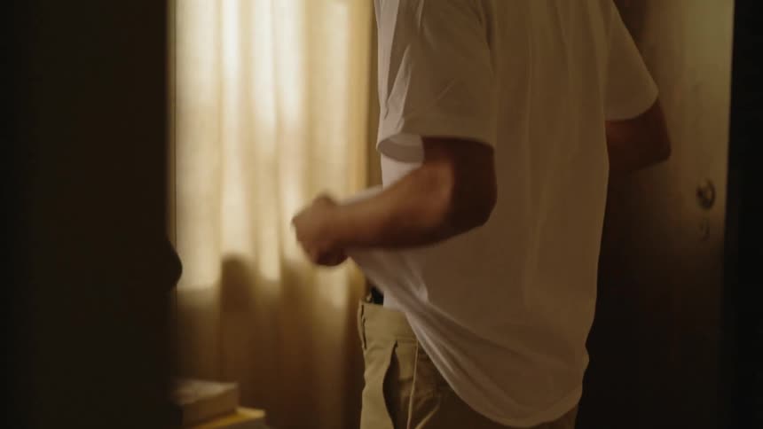 Man puts a gun in his waistband as he stands near a window