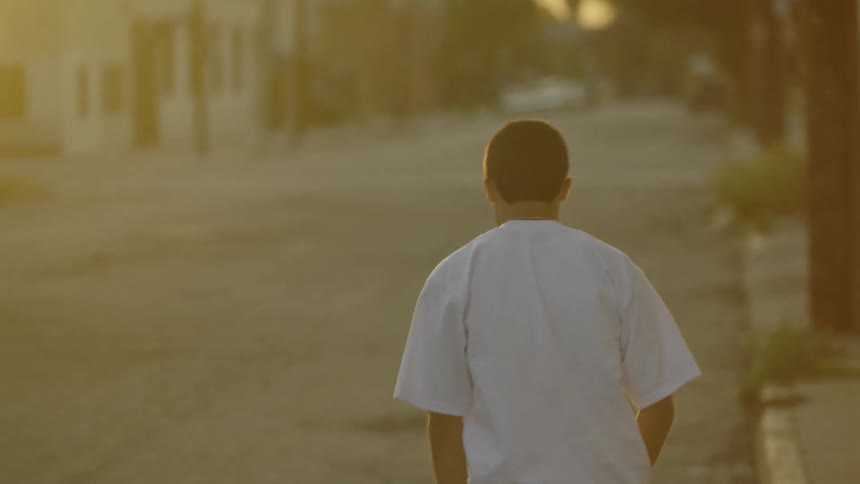 A boy crosses the street at sunset