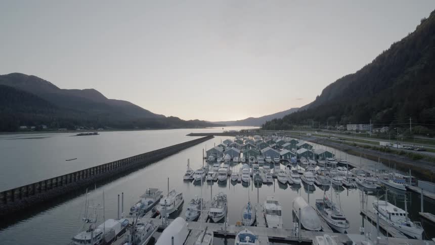 Boats and yachts sit docked in a harbor near the mountains
