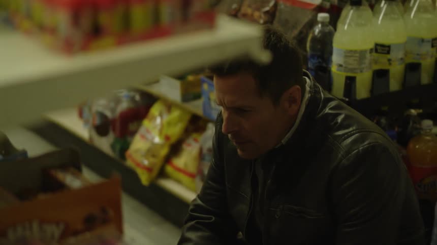 A man is crouched near the shelves looking for groceries