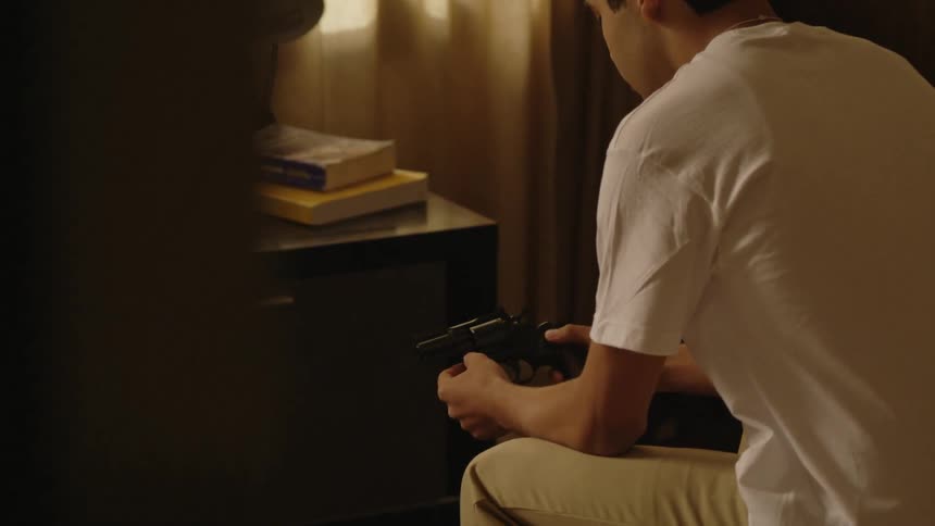 A boy holds a gun sitting on the bed