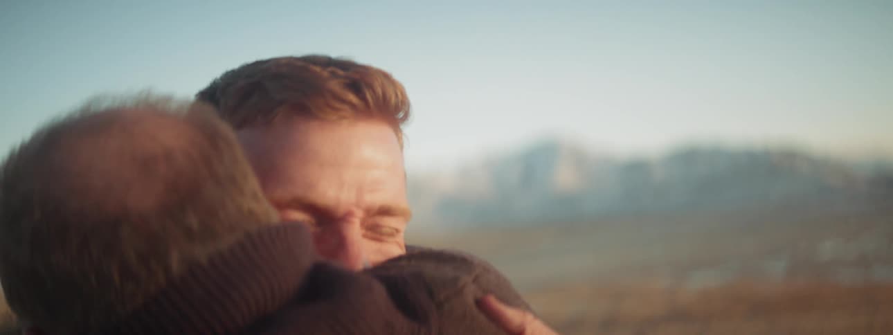 Two men hug near mountains at sunset