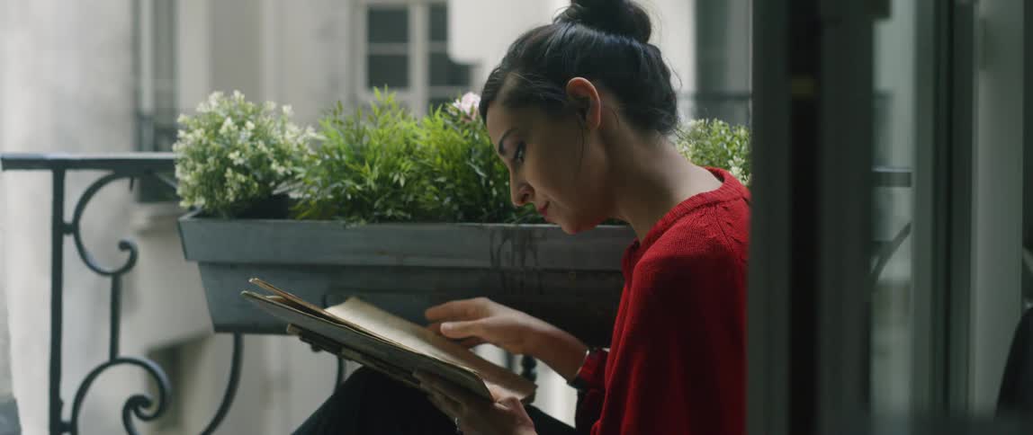 A woman slowly flips through her book near a bot on the terrace
