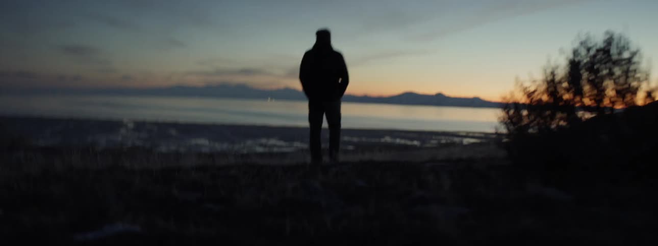 Man stands near a lake at dusk