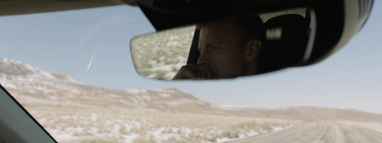 A man's face is reflected in the rear view mirror as he drives