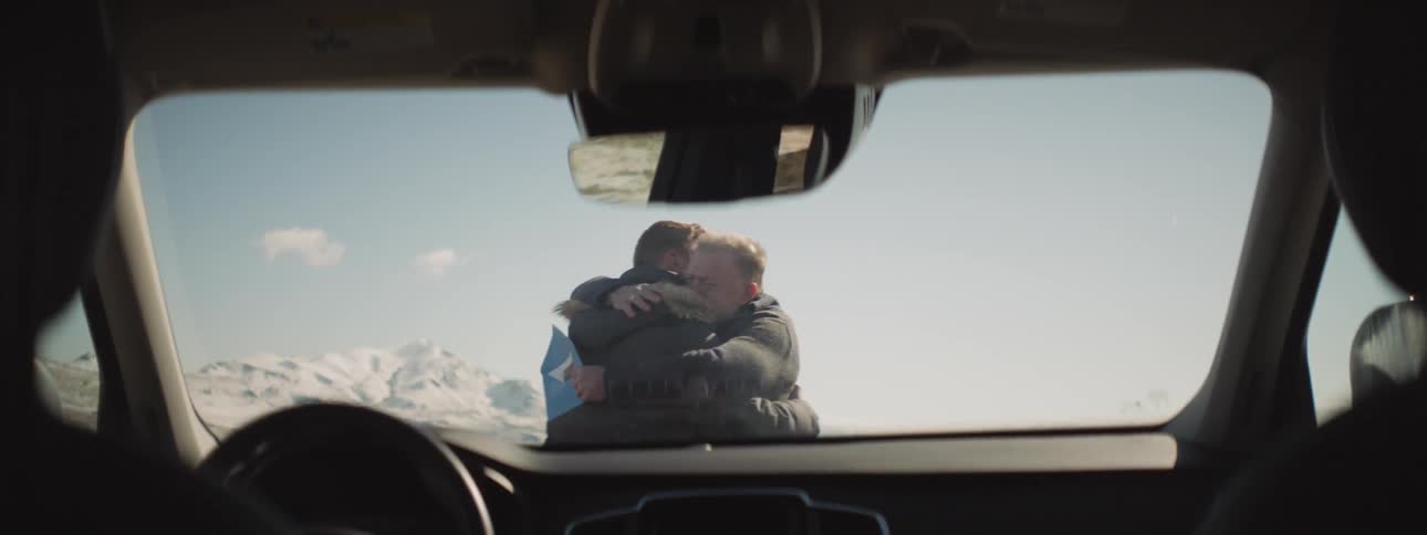 Two men hug while standing in front of a car