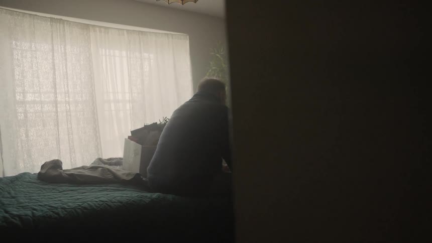 Man sits on a bed next to a cardboard box