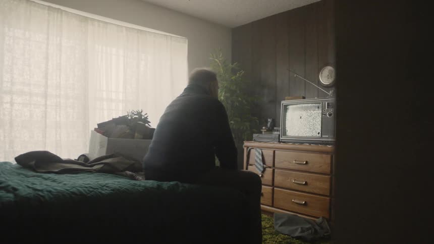 Man sits on the edge of the bed looking at the television
