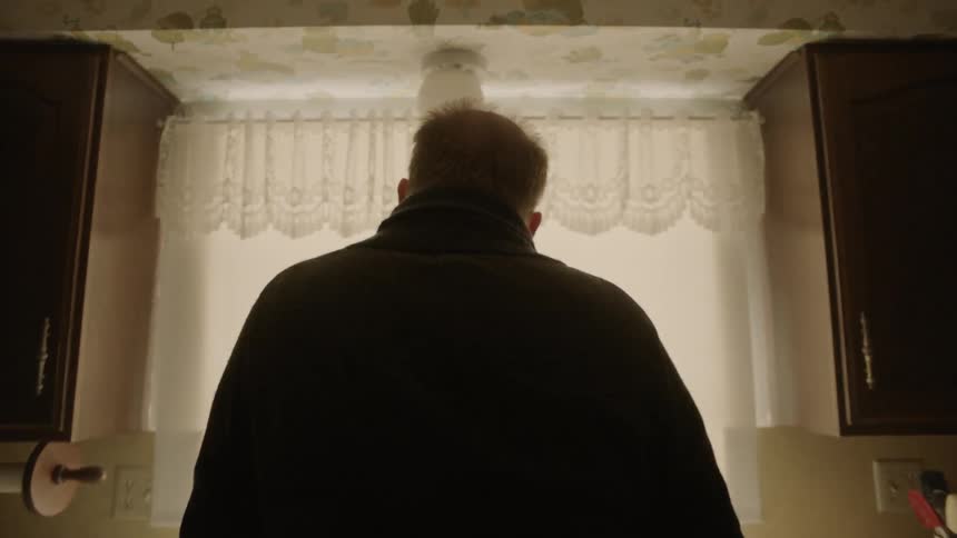 A man leans against the counter and looks out the kitchen window