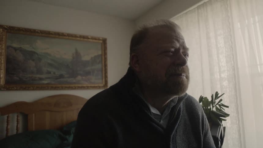 An elderly man sits on the bed